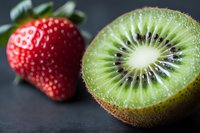 Fresh ripe strawberry and halved kiwi fruit showing detailed texture and seeds on dark background, macro food photography with selective focus.