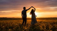 Romantic couple dancing in golden wheat field at sunset with dramatic sky. Man and woman silhouettes enjoying intimate moment in rural countryside landscape.