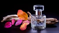 Elegant crystal perfume bottle with geometric pattern on dark background alongside vibrant autumn leaves and driftwood creating luxurious fragrance composition.