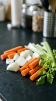 Fresh chopped vegetables including carrots, onions, celery and parsley arranged on dark kitchen counter ready for cooking soup or stew preparation.