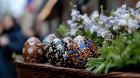 Decorated Easter eggs with intricate traditional patterns in brown and blue colors nestled among delicate spring flowers and green foliage in rustic basket setting.