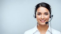 Friendly female customer service representative with headset smiling at camera in white shirt against gray background for business communications.