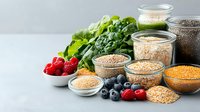 Fresh organic superfoods with berries, grains, seeds in glass jars and bowls on light background. Raw vegan ingredients for healthy eating and nutrition.