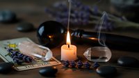 Mystical fortune telling setup with burning candle, tarot cards, crystal ball and lavender flowers creating atmospheric divination scene for spiritual practices.