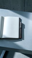 Open notebook with blank pages and pen on light surface with concrete wall background, suitable for business planning, education, writing projects, and creative work concepts.