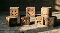 Wooden emotion blocks with carved smiley faces showing different expressions arranged on rustic surface for emotional intelligence and mindfulness concepts.
