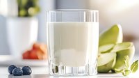 Fresh glass of milk with blueberries and sliced green bananas on white table, healthy breakfast concept with natural ingredients and morning light.