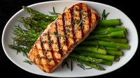 Grilled salmon fillet with fresh asparagus and rosemary herbs on white plate. Healthy protein meal with green vegetables for restaurant menu design.