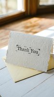 Handmade thank you card with stamped text resting on a yellow envelope in warm natural light on a wooden surface.