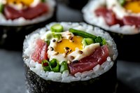 Fresh sushi roll with raw tuna, egg yolk, green onion and sesame seeds on dark background. Close up macro shot of Japanese cuisine with selective focus.