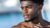 Young African American male model with confident expression against blurred blue background, natural lighting highlights defined features and groomed facial hair.