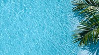 Bright turquoise swimming pool water surface with sunlight reflections and palm tree leaves in corner, creating tropical summer vacation atmosphere. Fresh aqua background.