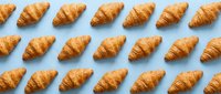 Freshly baked croissants arranged in rows on light blue background, overhead flat lay composition for bakery, food and breakfast design projects.
