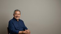 Middle-aged man with gray hair and mustache wearing navy blue shirt, seated against neutral background, suitable for corporate portraits and professional headshots.