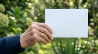 Senior male hand holding blank white card outdoors with green foliage background, suitable for advertising, messaging, and promotional campaigns.