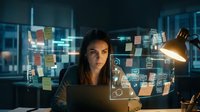 Young businesswoman working late at night with holographic digital interface displaying data analytics and virtual screens in modern office environment.