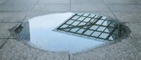 Puddle reflecting metal grid framework on urban pavement surface, suitable for conceptual and architectural photography projects.