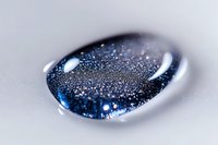 Sparkling blue liquid droplet with glittering particles captured in macro photography against white background shows cosmic-like texture and reflective surface.