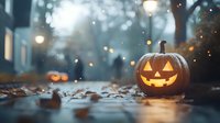 Glowing jack-o-lantern pumpkin on autumn street with fallen leaves at dusk, creating spooky Halloween atmosphere with bokeh lights in background.