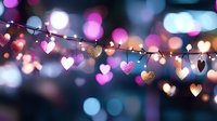 String of glowing heart-shaped lights against blurred bokeh background in pink and blue tones creates romantic festive atmosphere for Valentine's Day celebrations.