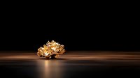 Crumpled gold foil ball on dark wooden surface with dramatic lighting and reflection, minimalist luxury composition against black background.