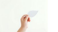 Hand holding blank white leaf-shaped paper against neutral background, suitable for eco-friendly branding, environmental messaging, sustainability concepts, and green business marketing materials.