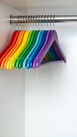 Colorful rainbow clothes hangers arranged on chrome closet rod creating vibrant spectrum from red to purple for organized wardrobe storage and home organization.