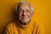 Senior Caucasian man wearing yellow knit sweater smiling warmly against vibrant yellow background, expressing joy and contentment in studio portrait setting.