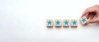Hand placing wooden blocks with blue stars in row for customer rating and feedback evaluation on white background with copy space.
