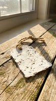 Handmade pumice stone with natural twine cord lying on rustic wooden floor near sunlit window, spa and wellness skincare product for foot care and exfoliation.
