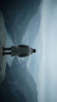 Solitary businessman in suit standing on rocky cliff edge against dramatic stormy sky with dark clouds for corporate challenge and determination concepts.