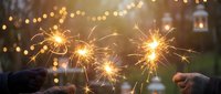 Hands holding lit sparklers with golden bokeh lights and festive atmosphere in blurred background, suitable for holiday celebrations and New Year events.