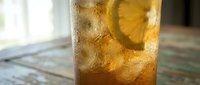 Refreshing iced tea with lemon slice in a tall glass, condensation drops on surface, served on rustic wooden table in natural light.