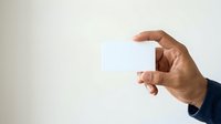Close-up of male hand holding blank white business card against neutral background, ready for branding and corporate design projects.