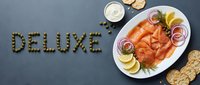 Deluxe smoked salmon platter with capers, red onion, lemon, dill, crackers, and cream cheese on dark slate, top view.