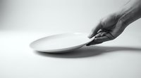 Hand holding a white empty plate on a light background, monochrome studio shot conveying minimalism, hunger, or clean dining concepts.