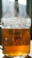 Steaming hot tea in a glass mug with Thank You inscription, warm golden liquid with condensation drops, cozy gratitude concept.