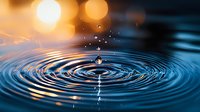 Mesmerizing water drop splash creating concentric ripples on blue water surface with golden bokeh lights and droplets frozen in motion against dark background.
