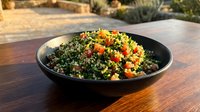 Tabbouleh salad with fresh parsley, tomatoes, and bulgur wheat served in black bowl on wooden table outdoors.