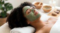 Young African American woman relaxing with green clay facial mask at spa, enjoying natural skincare treatment for wellness and self-care routine.