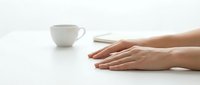 Female hands resting on clean white table surface next to coffee cup in minimalist workspace setting for relaxation and mindfulness concepts.