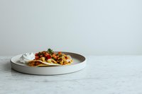 Mexican tostadas topped with seasoned meat, fresh cilantro served on minimal gray ceramic plate against white marble background.