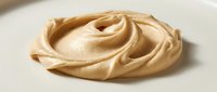 Creamy peanut butter swirl on white plate, smooth spread texture for food styling, cooking, and culinary design projects.
