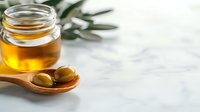 Golden honey in glass jar with wooden spoon and fresh olives on white marble surface. Natural organic food ingredients for healthy cooking and wellness.