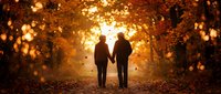 Two people holding hands walking down an autumn tree-lined path with golden bokeh lights and falling leaves creating a warm, romantic atmosphere.