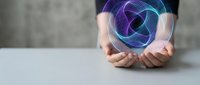 Hands holding glowing holographic geometric sphere with purple and blue neon wireframe pattern floating above palms against neutral background for technology concepts.