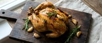 Golden roasted whole chicken with herbs and garlic on rustic wooden cutting board, perfect for holiday meals, family dinners and culinary presentations.