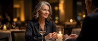 Elegant mature blonde woman enjoying romantic dinner date in upscale restaurant with candlelight ambiance and wine glasses for lifestyle content.