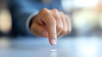 Close-up view of person's hand reaching to pick up small white pill or medication tablet against blurred background, medical and healthcare concept.