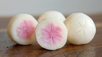 Traditional Japanese mochi desserts with pink cherry blossom design on wooden surface, showcasing delicate craftsmanship and cultural sweet treats.